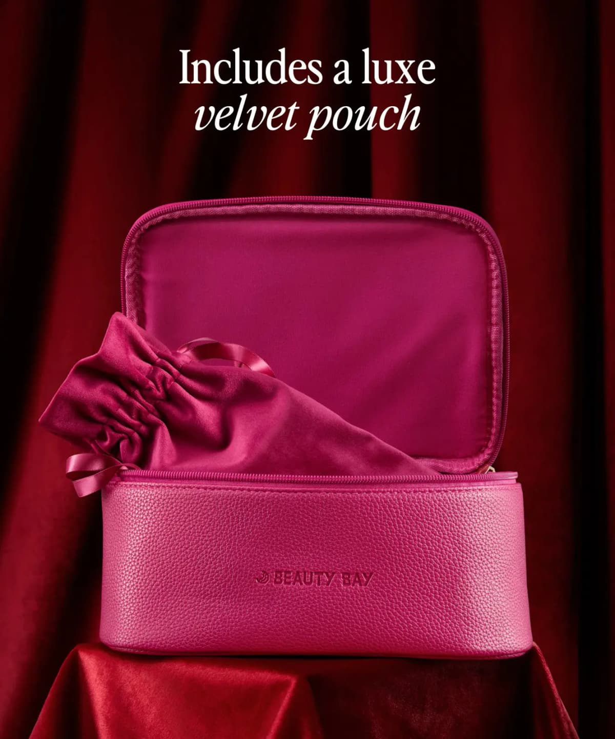 The Beauty Bag in pink pebbled faux leather, open with a pink velvet drawstring pouch inside, on red velvet