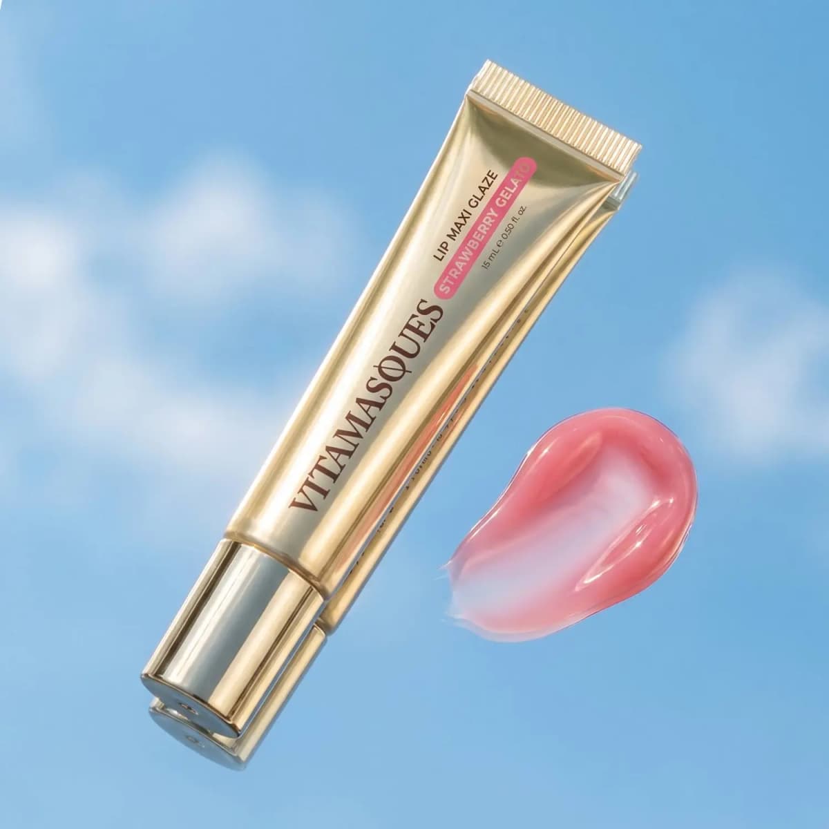 Gold Vitamasques Strawberry Gelato Maxi Glaze tube beside a glossy sheer pink swatch against a blue cloudy sky