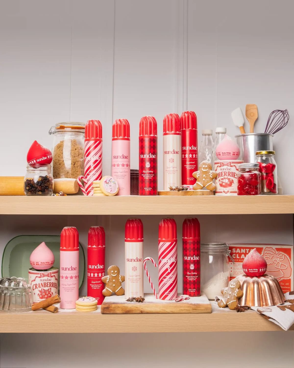 Sundae Body Holiday 2026 Collection whipped shower foams and Body Whips on wooden shelves with gingerbread and baking props
