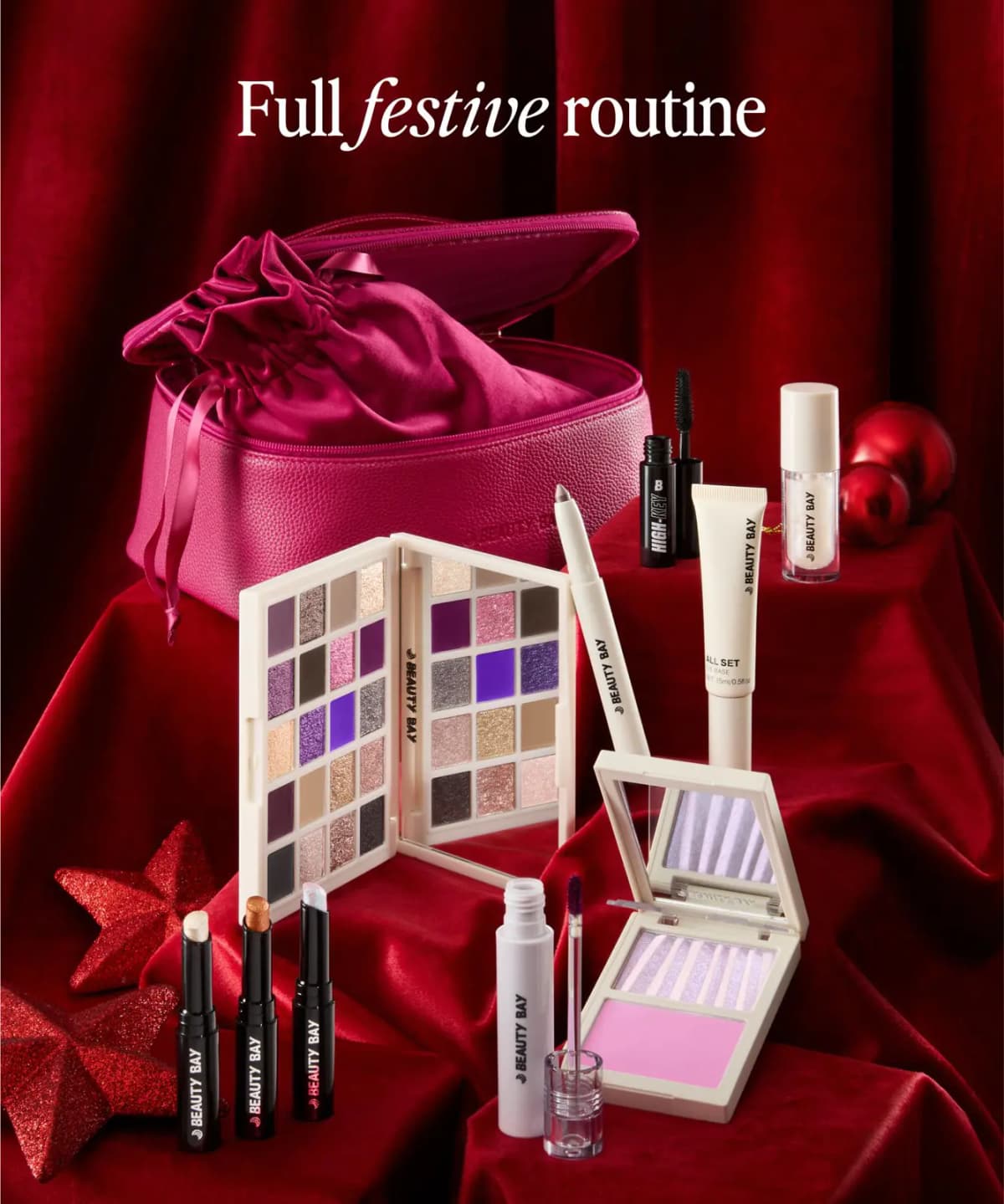 Kit contents on red velvet with open pink bag, velvet pouch, palette, mascara, lip stain and duo under 'Full festive routine
