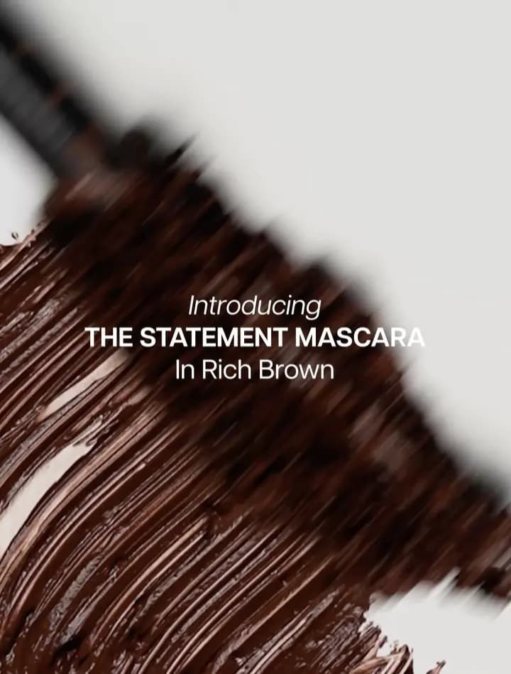 Rich brown mascara swatch smeared on white beside a blurred wand, text introducing The Statement Mascara in Rich Brown
