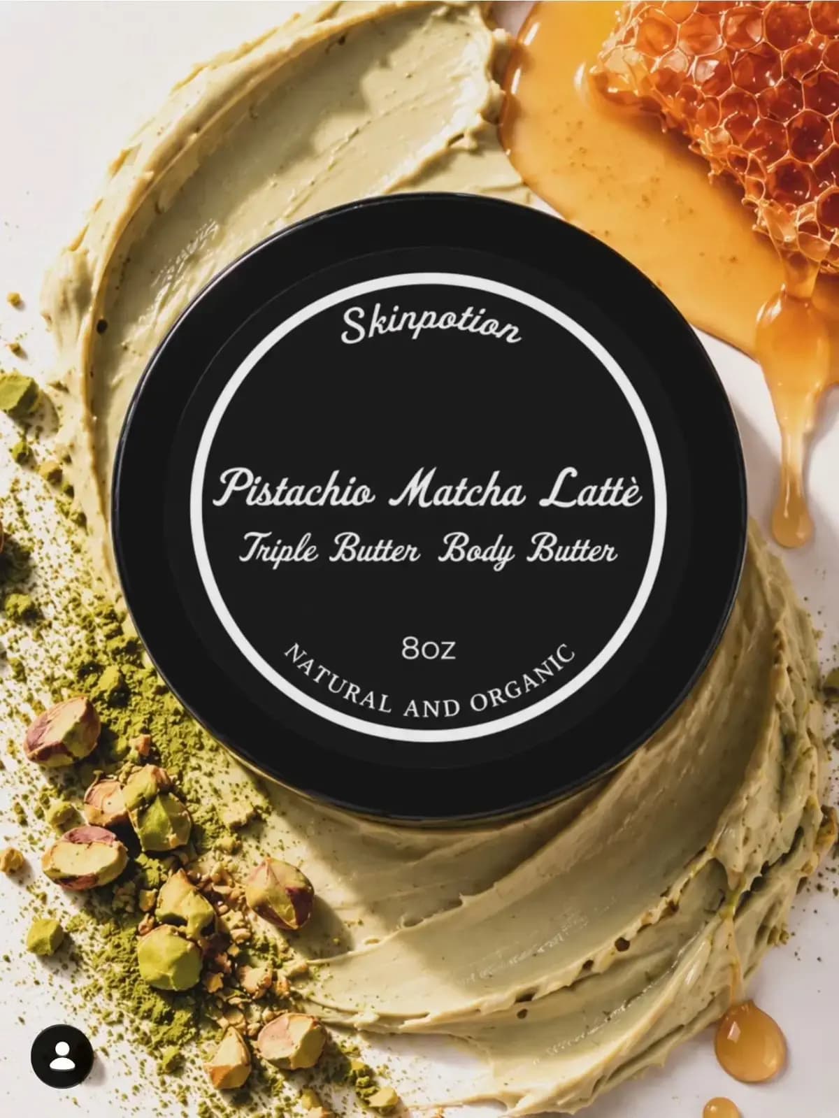 Black round tin of Triple Butter Body Butter on a pale green swirl of cream, with matcha powder, pistachios and honeycomb