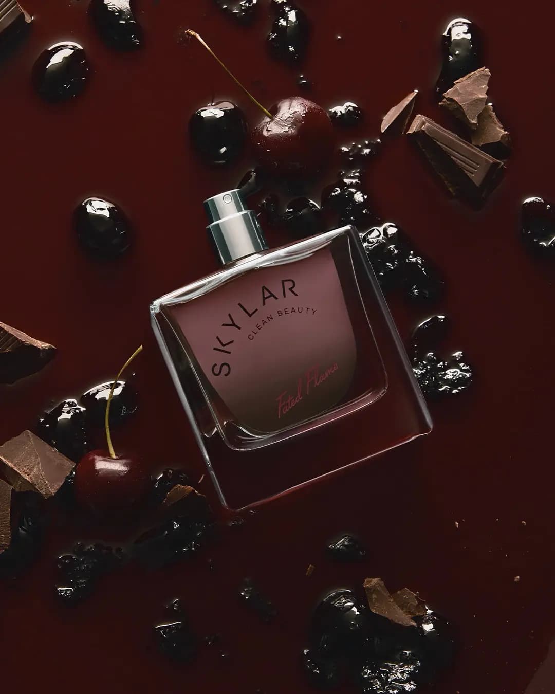Skylar Fated Flame square glass perfume bottle lying in glossy dark cherry syrup with fresh cherries and chocolate chunks