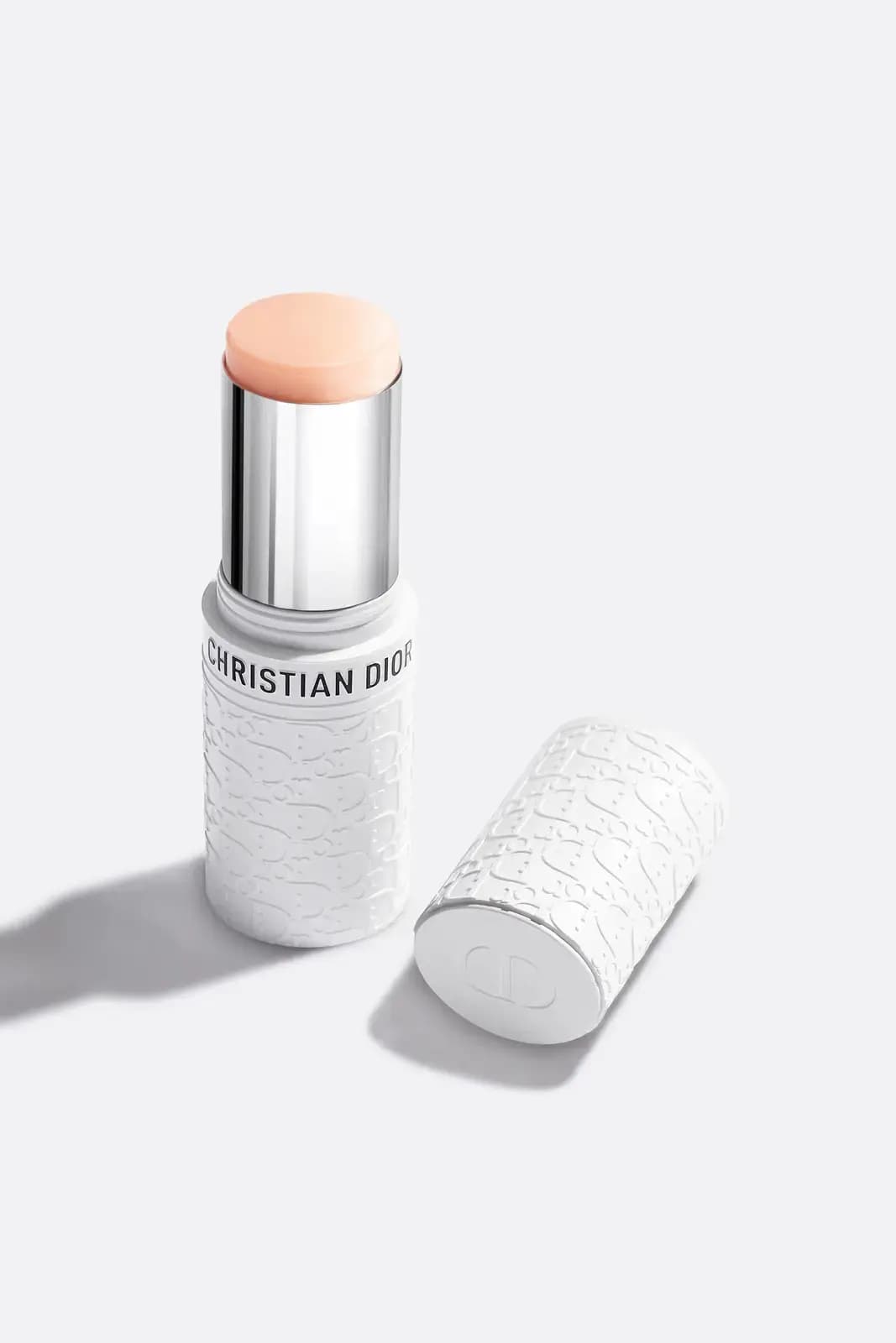 Uncapped stick with peach balm in a silver sleeve, its white embossed cap lying on its side