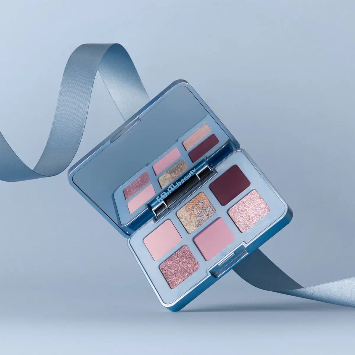 Open Prima Palette floating with a blue satin ribbon curling around it on a pale blue background.