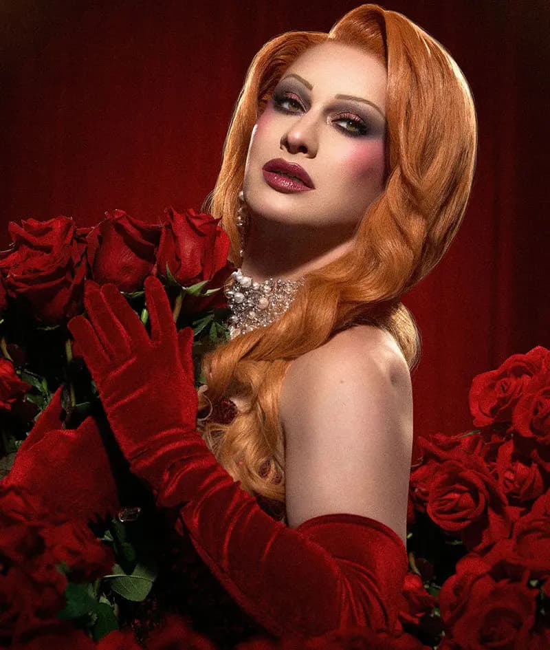Jinkx Monsoon in red velvet gloves and pearl choker holding red roses, wearing smoky eyes and berry lips