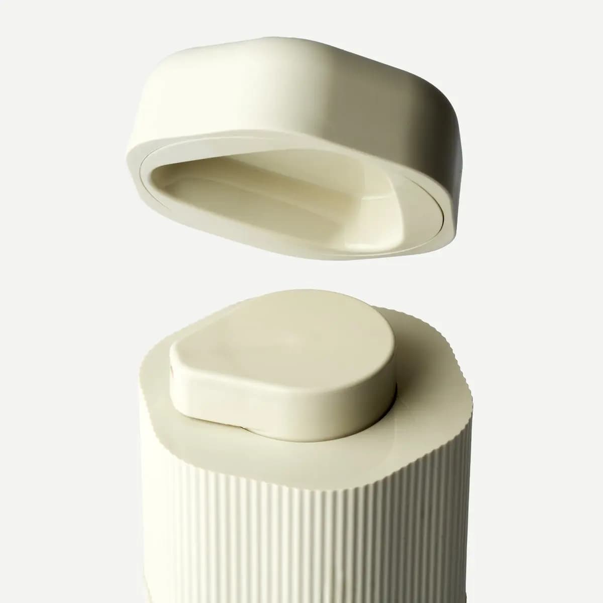 Close-up of a cream oval travel cap lifted above a retracted ribbed pump top