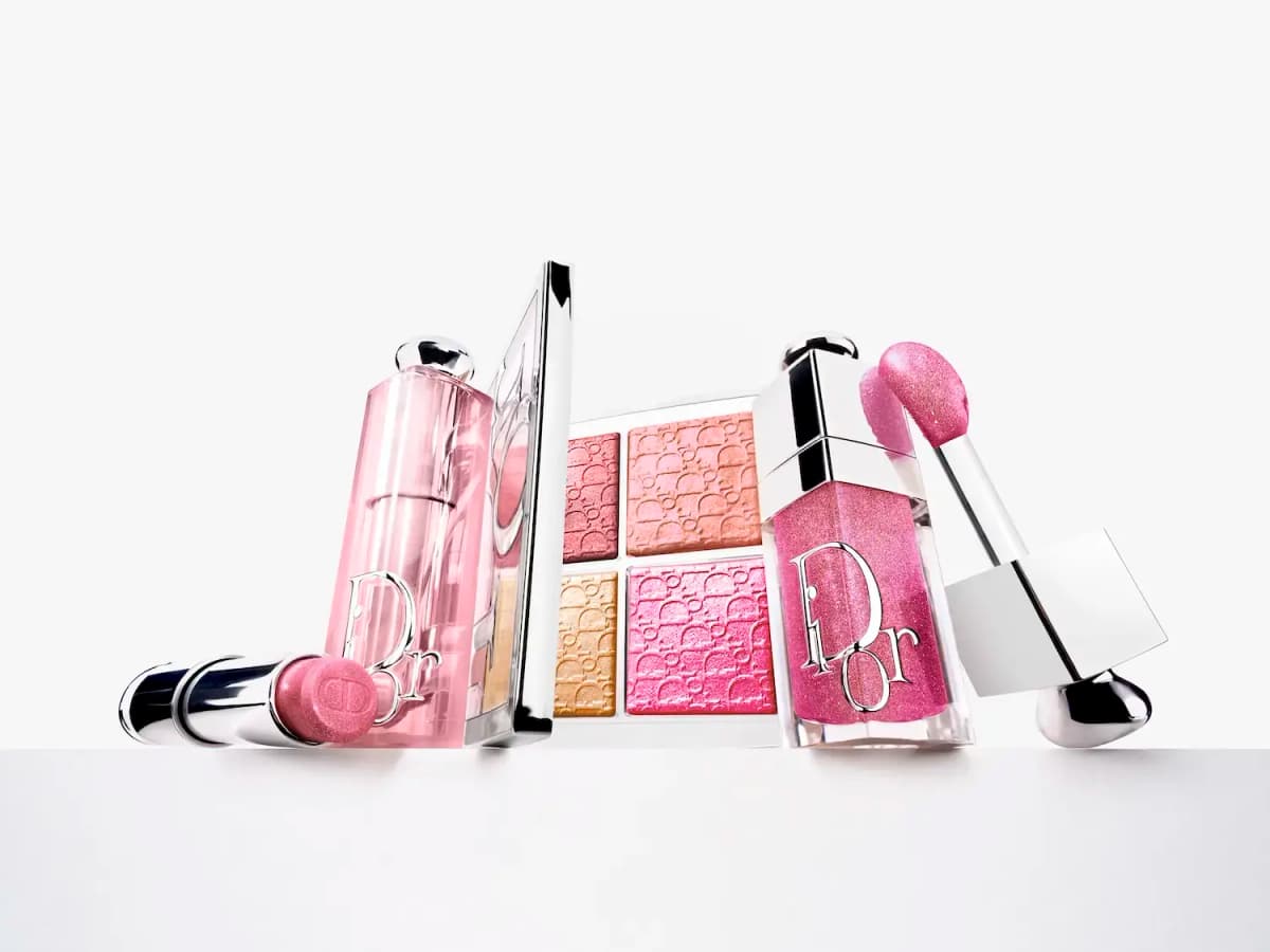Dior lipstick, pink lipstick case, glow palette and glittery pink lip oil with applicator on a white ledge
