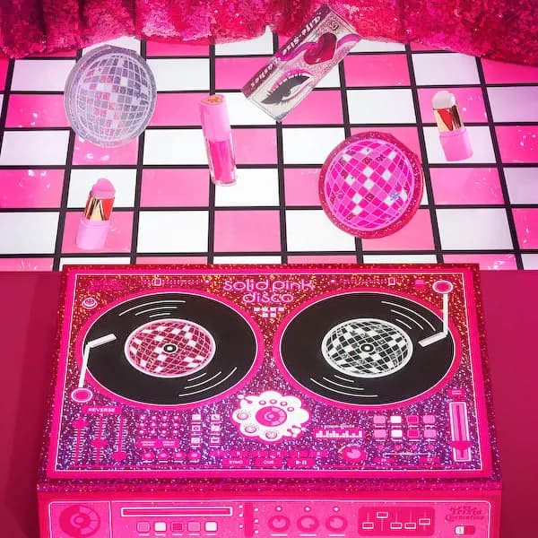 Trixie Cosmetics Solid Pink Disco collection with a pink DJ turntable PR box, disco-ball highlighter and lip gloss on a checkered floor