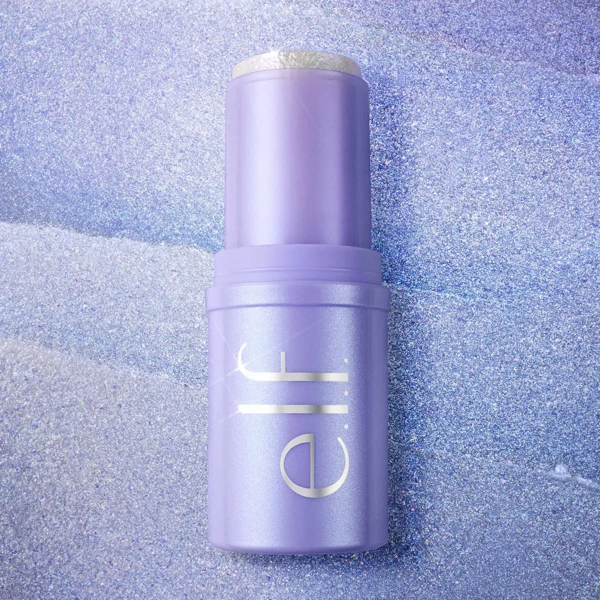 Lilac e.l.f. hair stick lying on a shimmering blue and lavender glitter surface.
