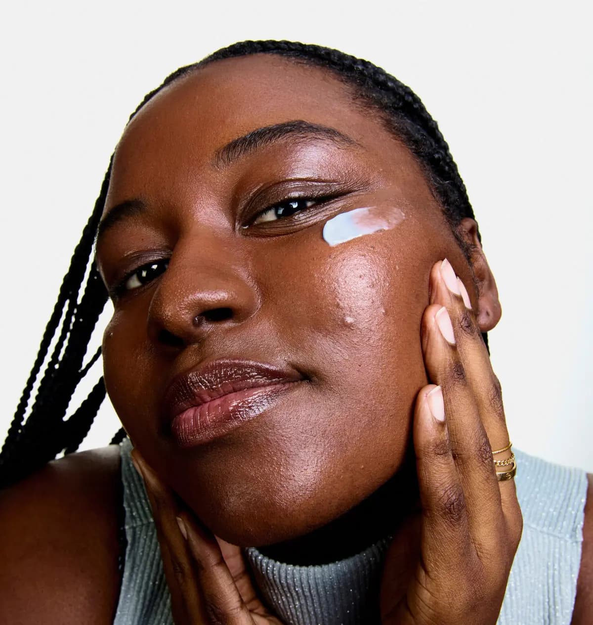Woman with braids cradling her face, a stripe of pale blue moisturiser across her cheekbone
