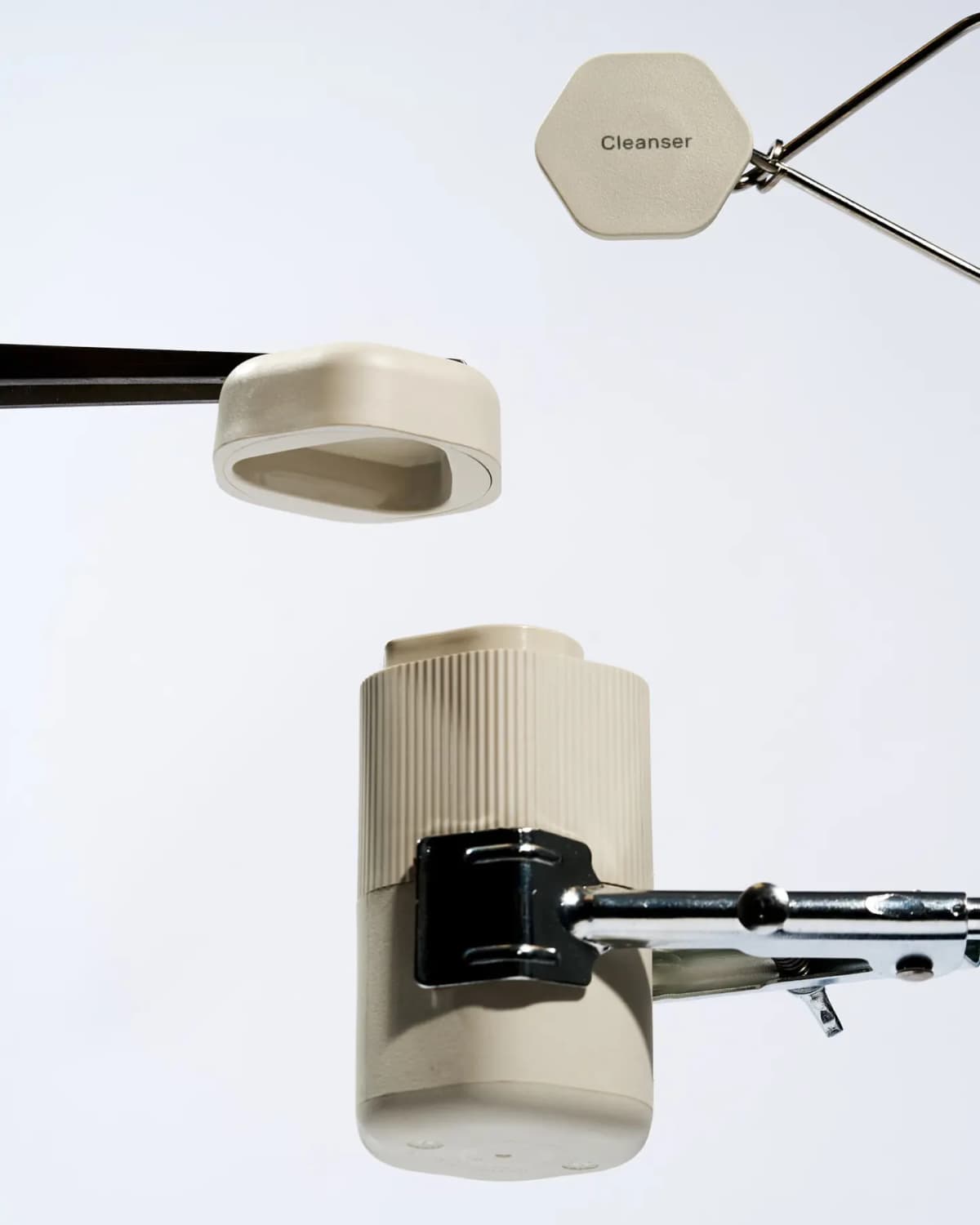 Pump Capsule held in a metal clamp beside a floating cream cap and a hexagonal 'Cleanser' label tag