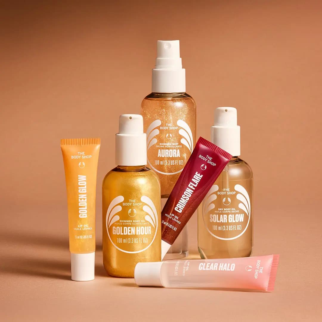 The Body Shop Glow Collection body oils, Aurora shimmer mist and three lip oil tubes grouped on a terracotta backdrop