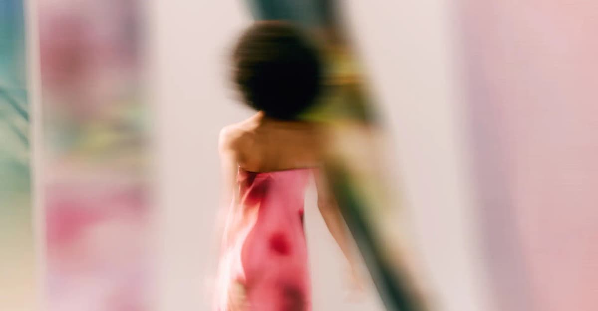 Motion-blurred figure in a strapless pink floral dress seen from behind against a soft pink and green backdrop