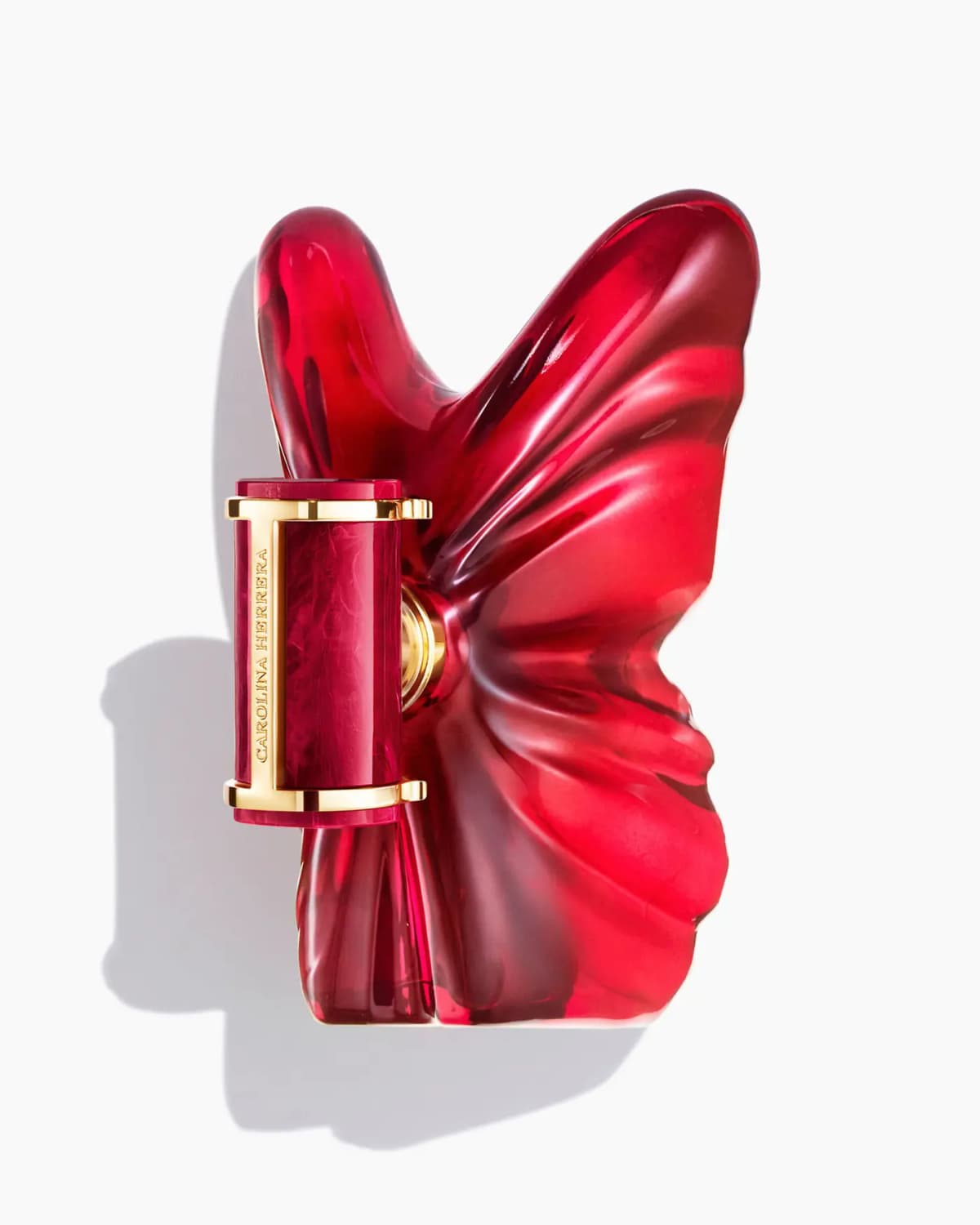 Top-down view of the red glass butterfly bottle with Carolina Herrera engraved gold and marbled red cap, casting a shadow
