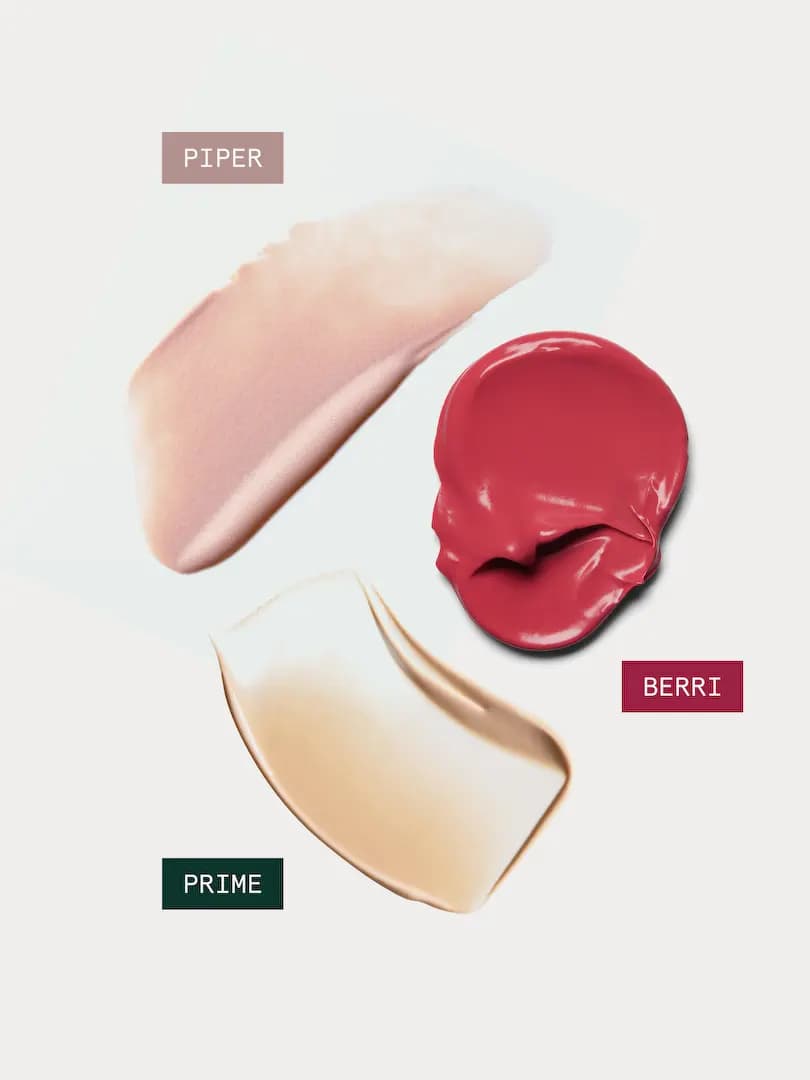 Swatches of shimmery pink Piper highlighter, glossy red Berri blush and beige Prime primer on a pale background