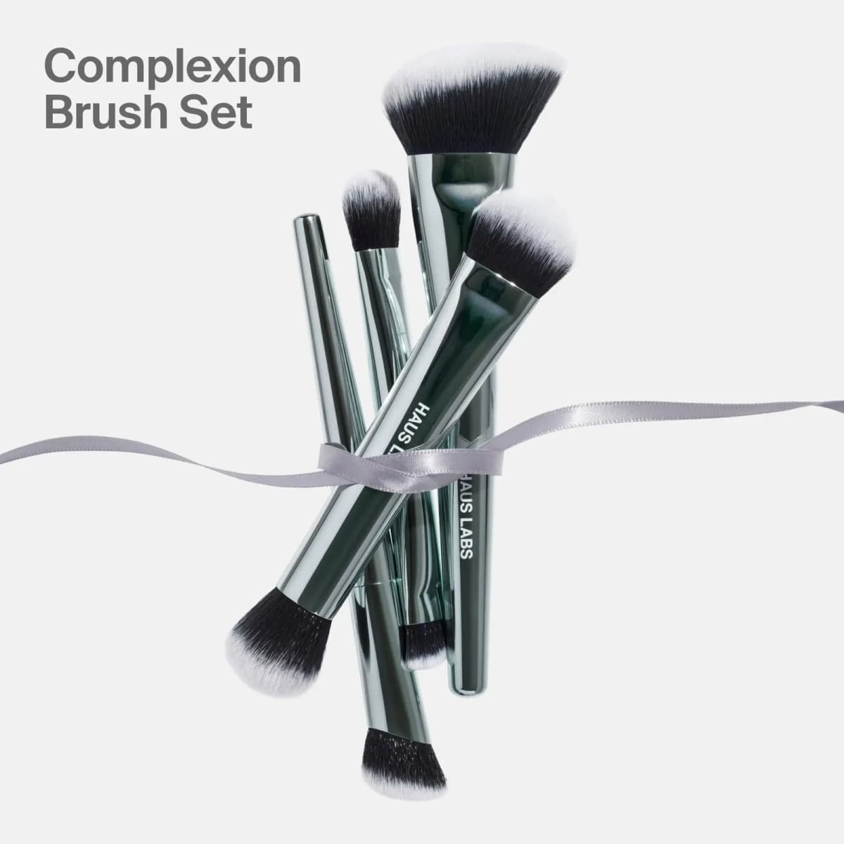 Four metallic green Complexion Brush Set brushes bundled together with a lilac-grey satin ribbon