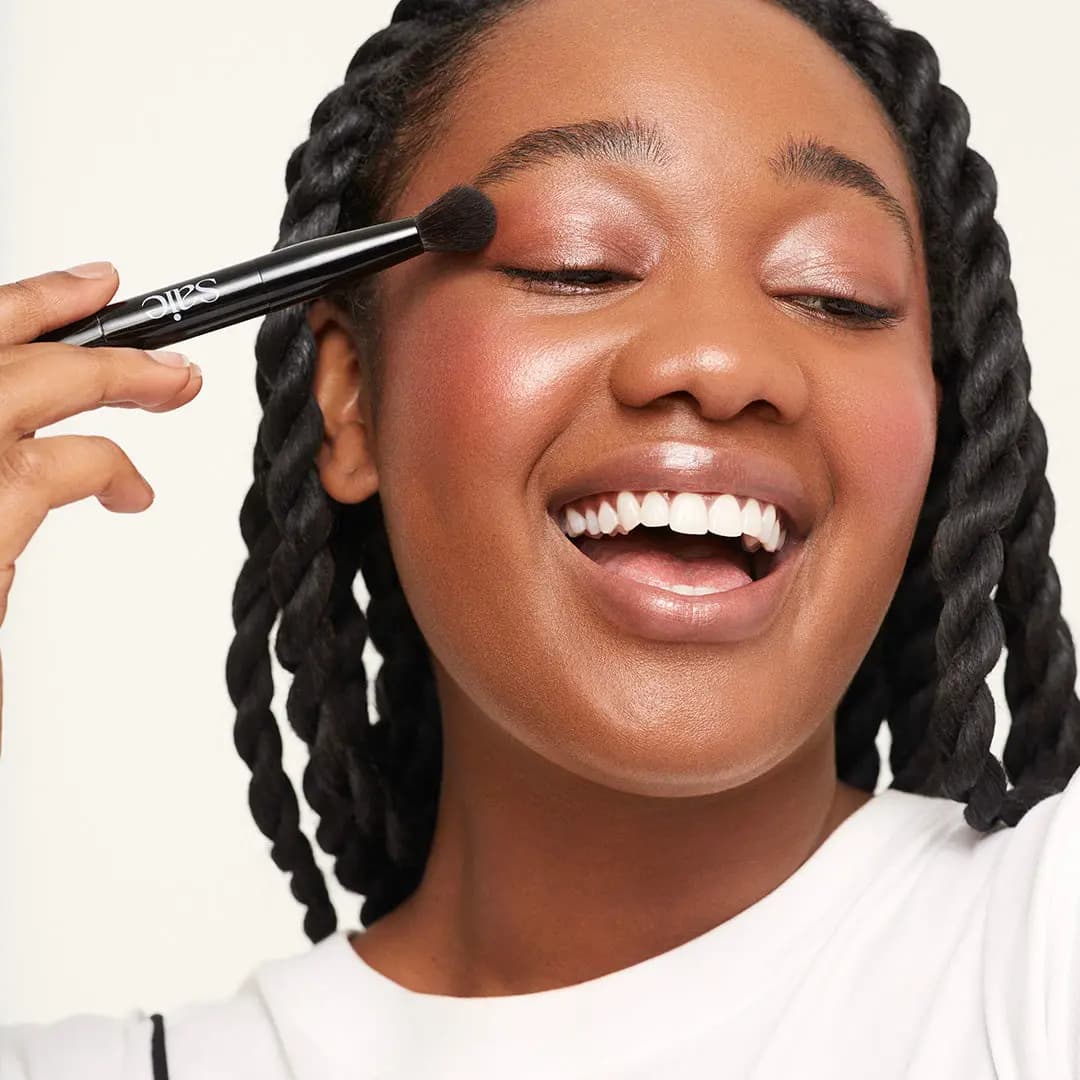 Smiling model with braids sweeping pink shadow on the eyelid with a small Saie brush