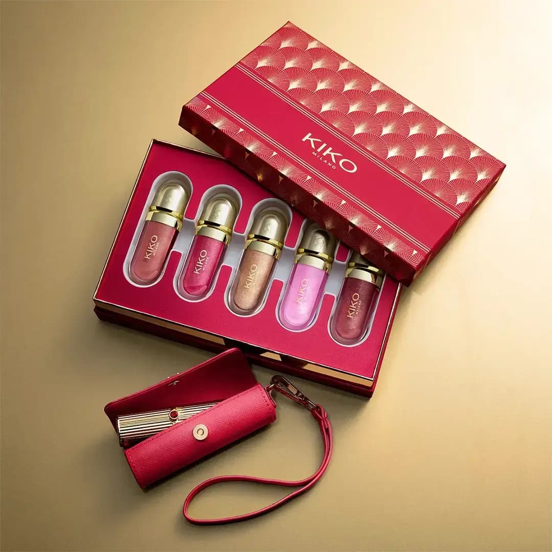 Open red KIKO box holding five glittery lip glosses in pink, berry and gold, with a red leather lipstick case