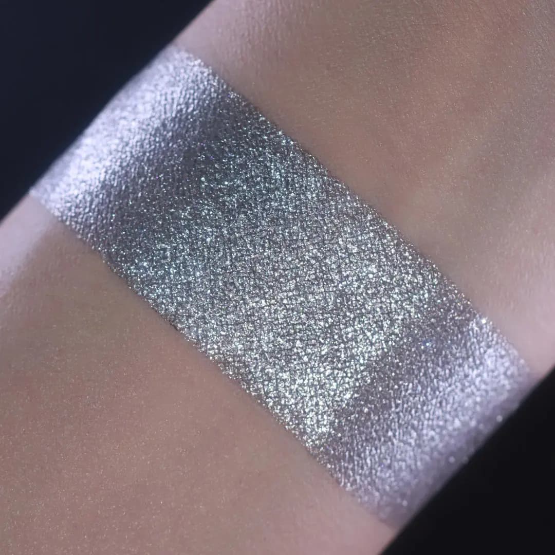 Wide arm swatch of a silver-grey metallic shimmer with a cool lilac sheen against bare skin on a dark background.
