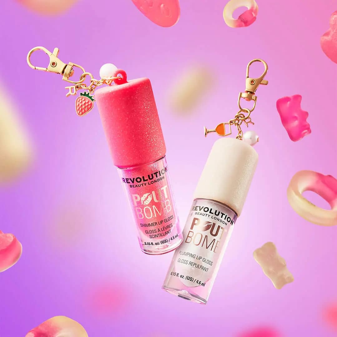 Pink-capped and white-capped Pout Bomb lip glosses with gold charms floating among blurred gummy sweets