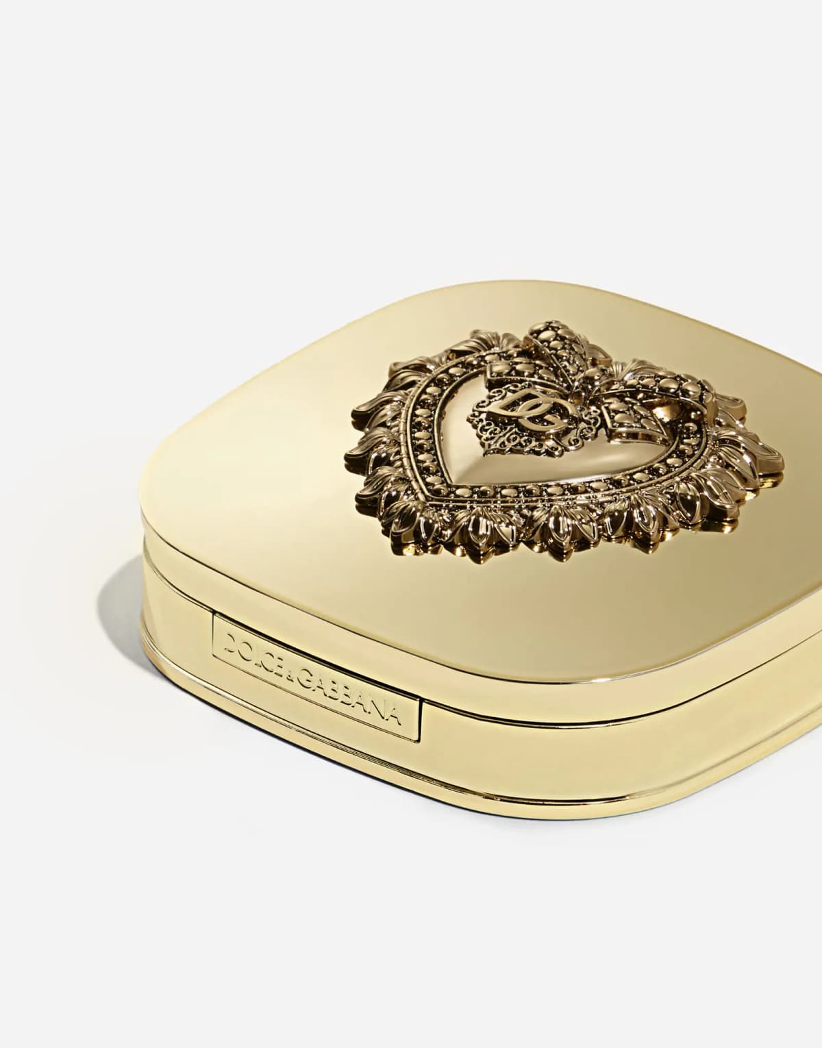 Angled closed gold compact showing the sculpted heart lid and an engraved Dolce&Gabbana side plate