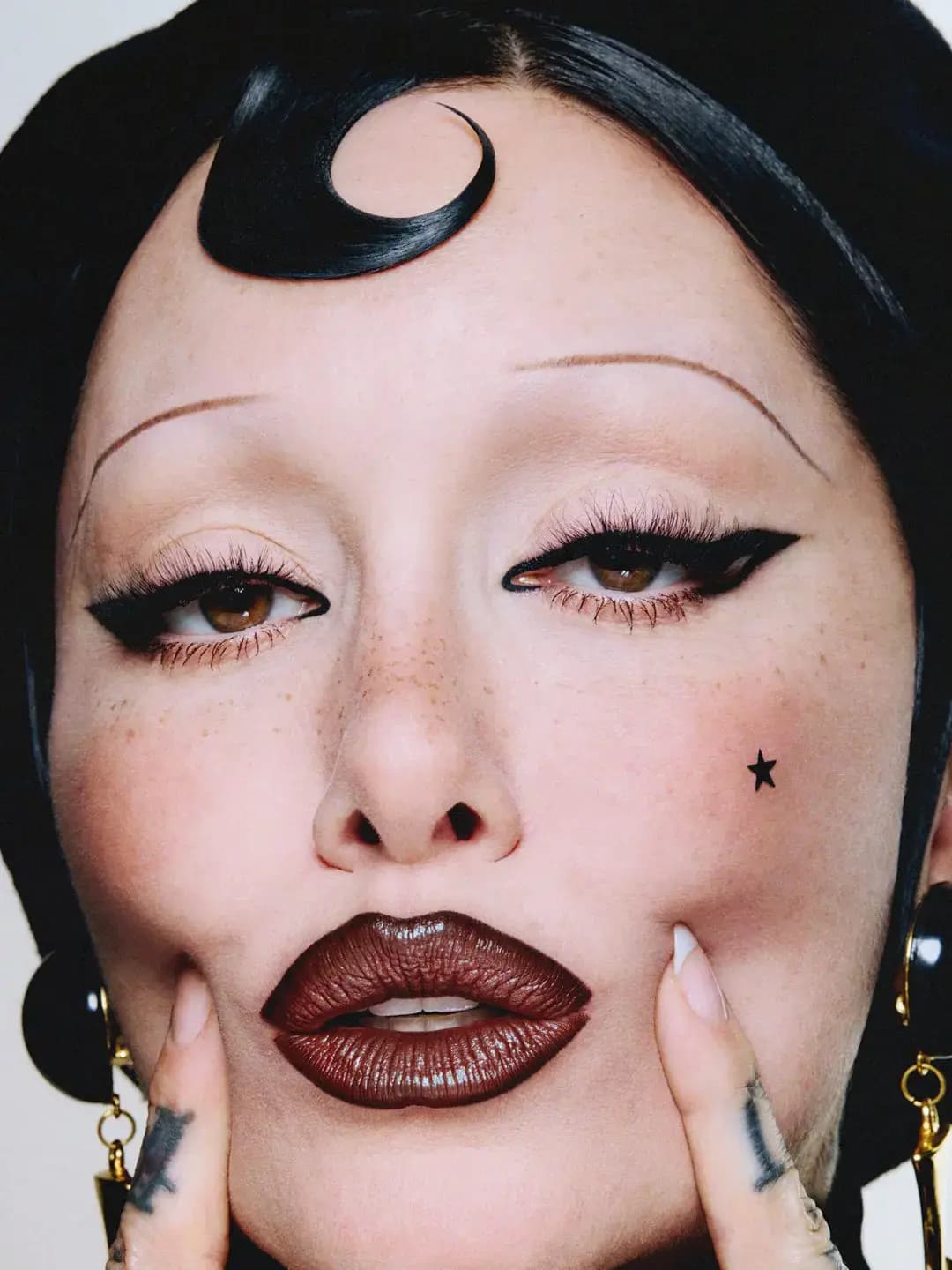 Close-up of Erin Parsons in winged liner and freckles wearing glossy deep brown Frost Lipstick in Spanish Fly, fingers framing the lips