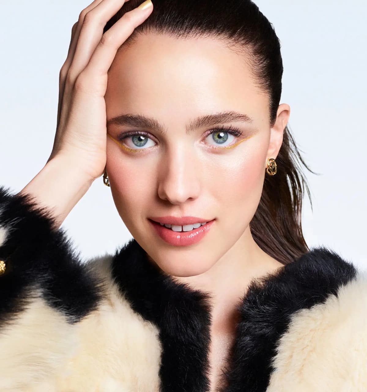 Margaret Qualley in a cream and black fur collar, hand to her hair, in Chanel's Holiday 2026 makeup campaign