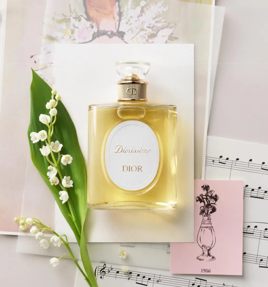 Diorissimo Dior perfume bottle on paper beside lily of the valley stems, sheet music and a pink 1956 sketch card.