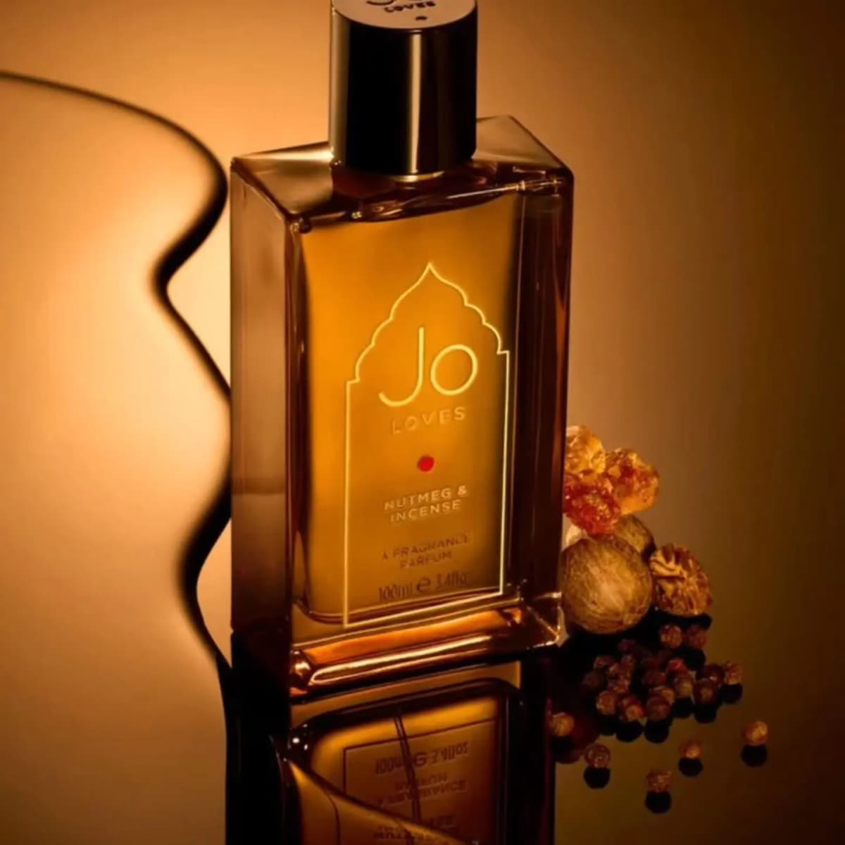 Angled Nutmeg & Incense bottle on a reflective surface beside resin, nutmegs and peppercorns in warm amber light