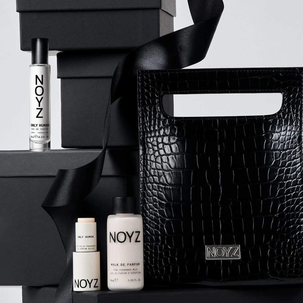 Only Human spray, solid stick and Mylk de Parfum styled with a black croc tote, stacked black boxes and satin ribbon