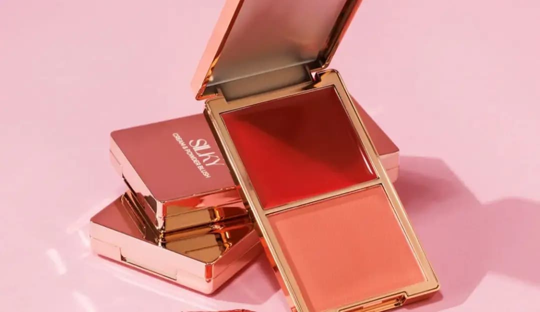 Open compact with deep red cream and peach powder blush resting on closed rose-gold Silky compacts