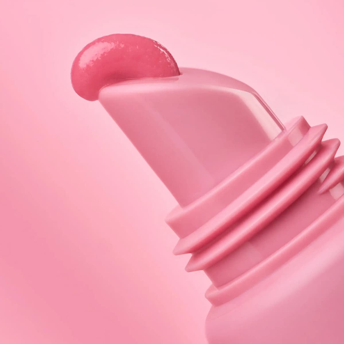 Macro of a glossy pink drop of lip mask on the angled tip of the pink tube