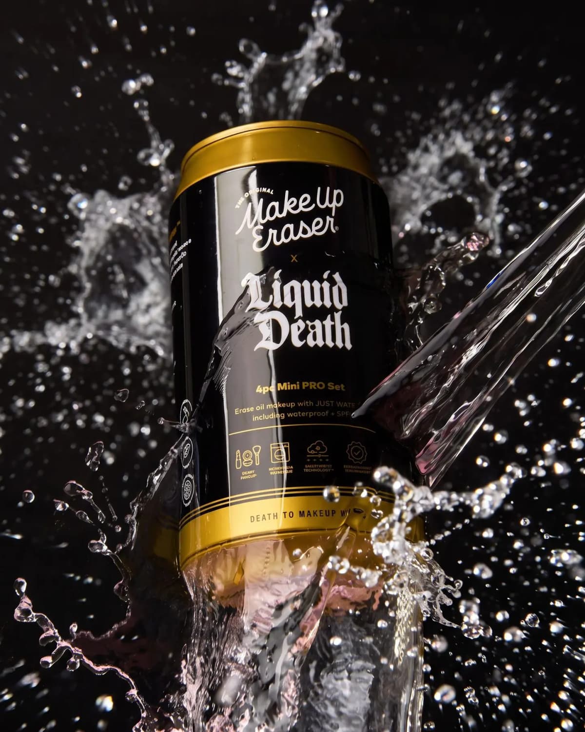 Black-and-gold MakeUp Eraser x Liquid Death 4pc Mini PRO Set can splashed by a stream of water on a black background
