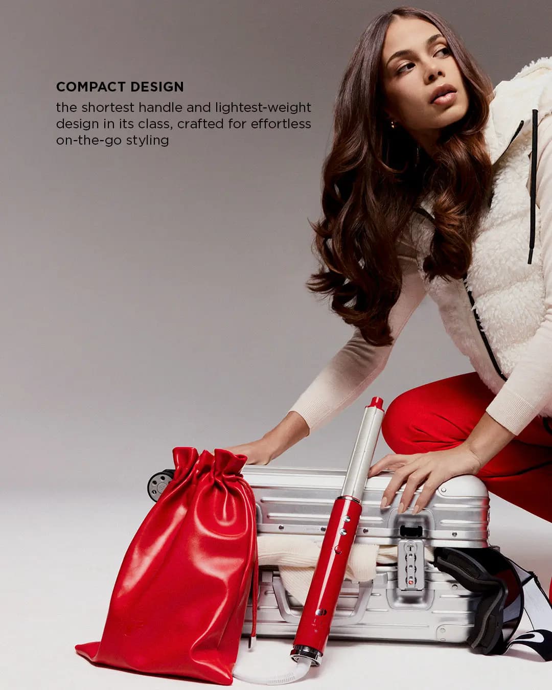 Model with voluminous curls packing a silver suitcase beside the styler and red tote, captioned Compact Design