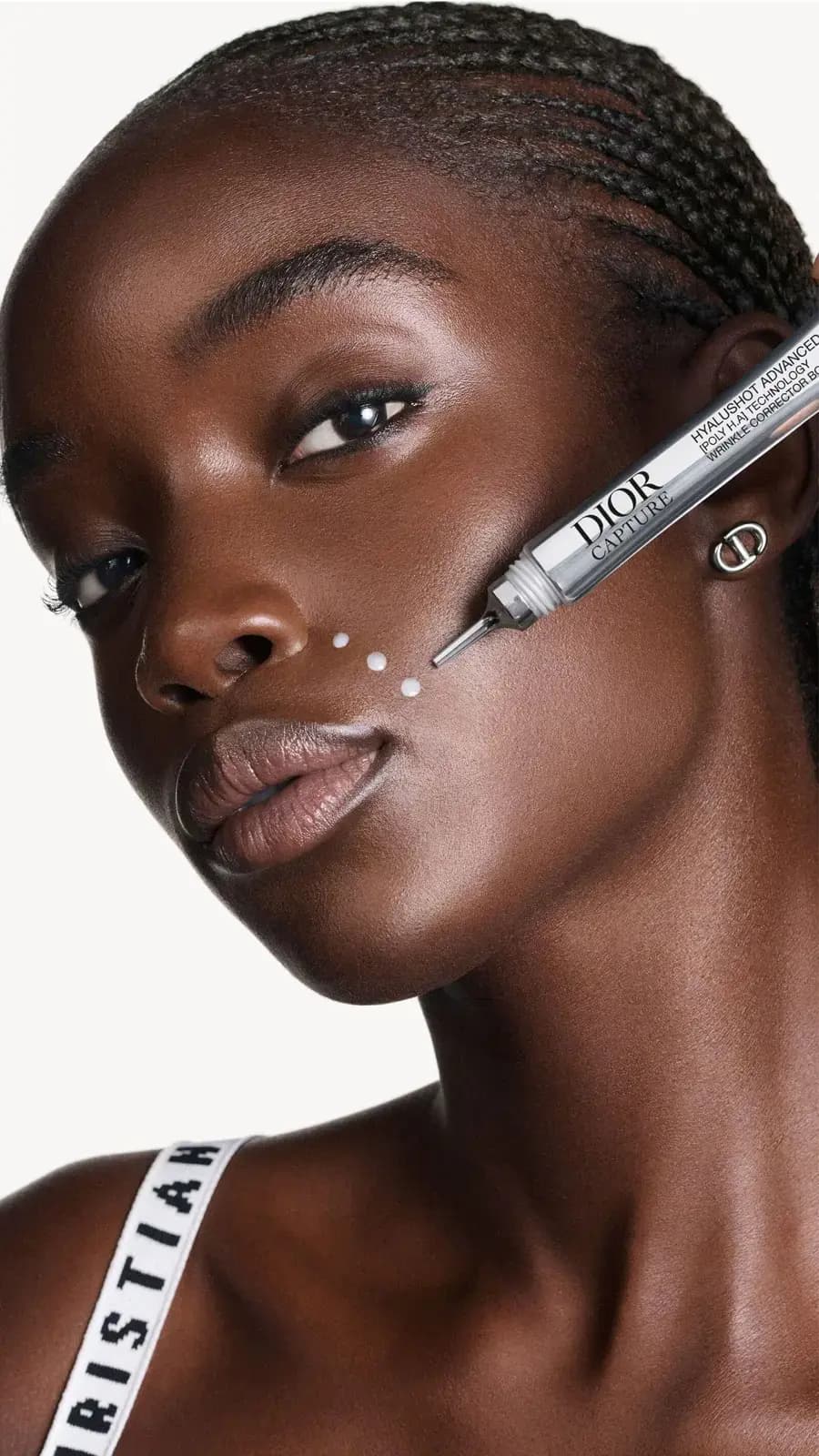 Model with braided hair and a Dior earring as the applicator dots product along her cheek beside the nose