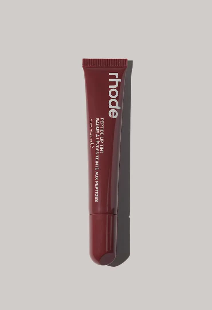 Deep burgundy-red rhode Peptide Lip Tint tube standing upright against a light grey backdrop