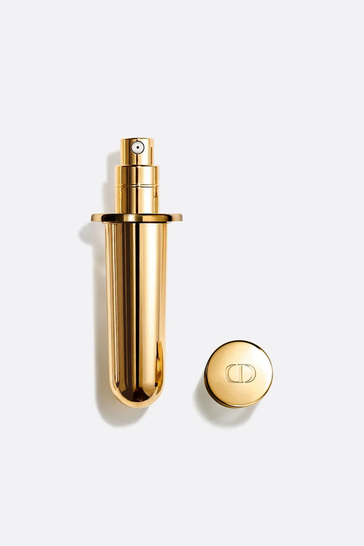 Gold refill vial with pump and flange next to a round gold CD-embossed cap on a light background