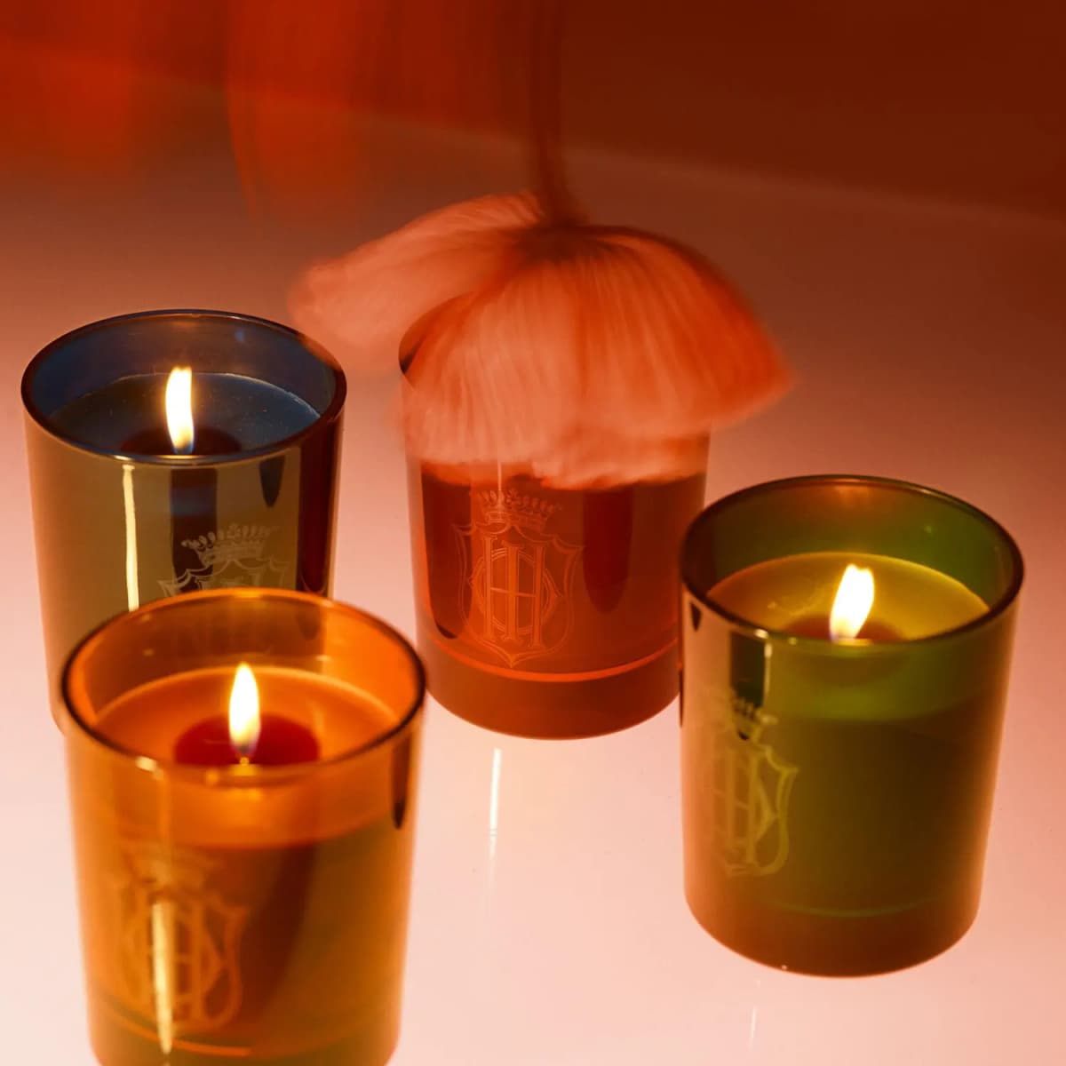 Four lit Sisley candles in blue, amber, orange and green glass with crest motifs, a pink tassel hanging above