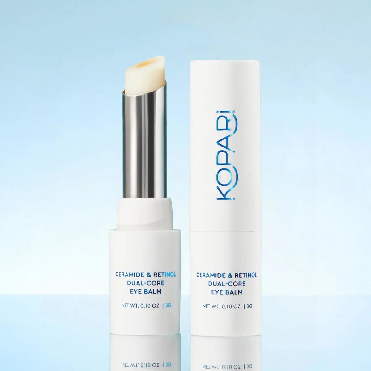Ceramide & Retinol Dual-Core Eye Balm uncapped to show a pale balm with yellow core in a silver sleeve beside its white cap