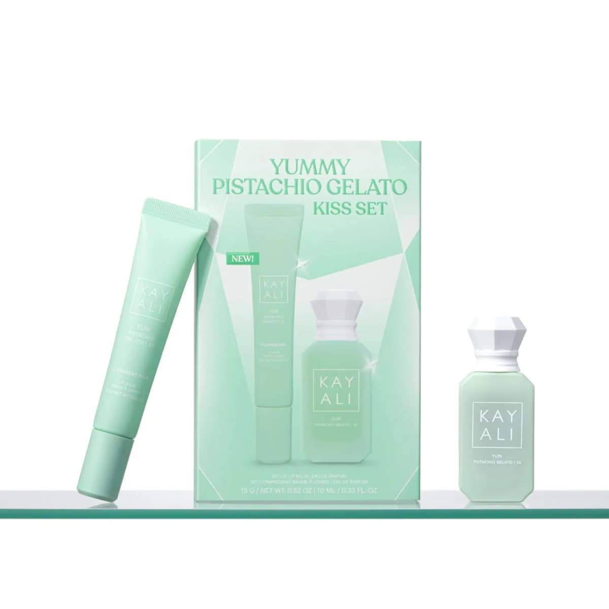 Mint lip balm leaning against the Pistachio Gelato Kiss Set box, with the perfume bottle on a glass shelf