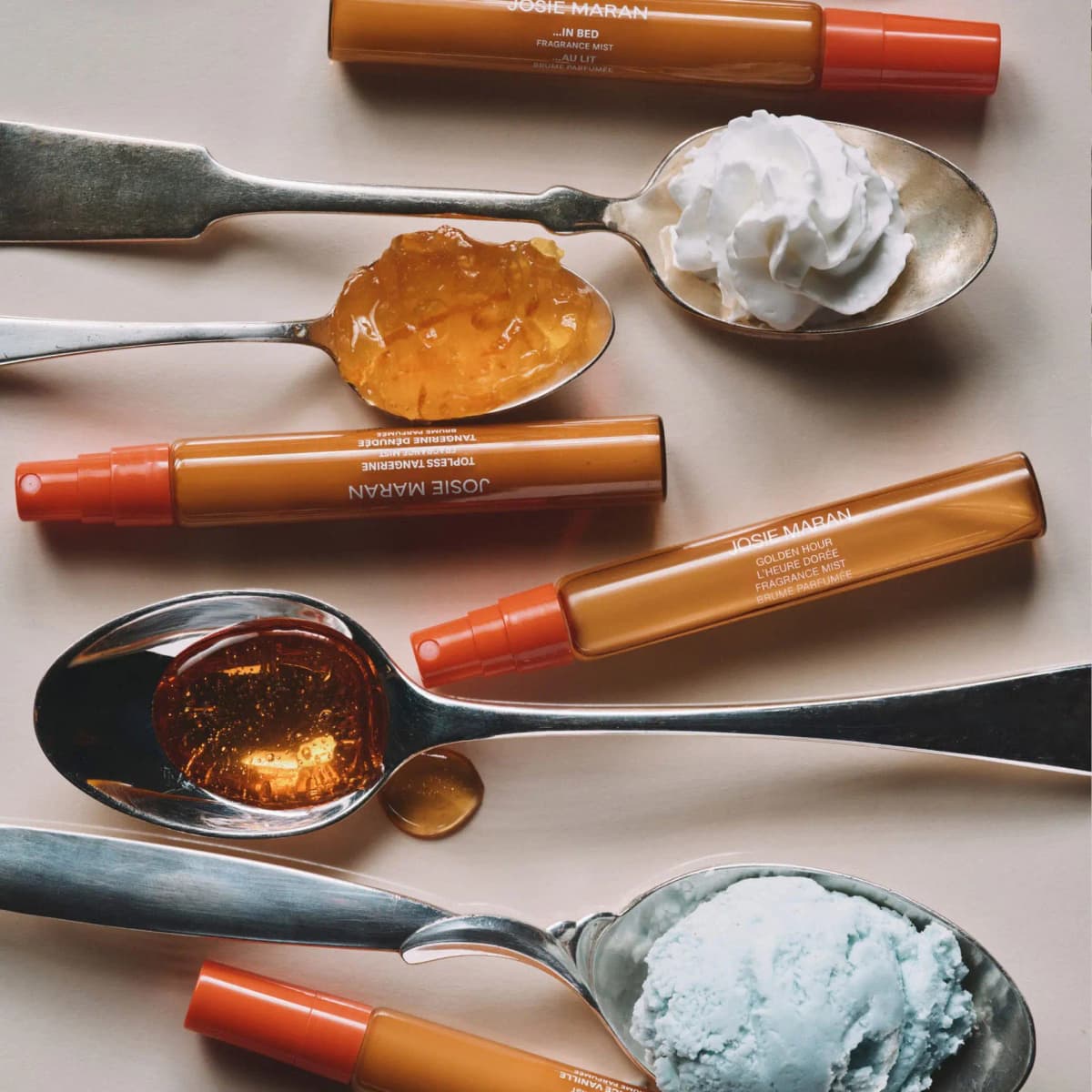Flat lay of Josie Maran mist tubes among spoons holding whipped cream, orange marmalade, honey, and mint ice cream.