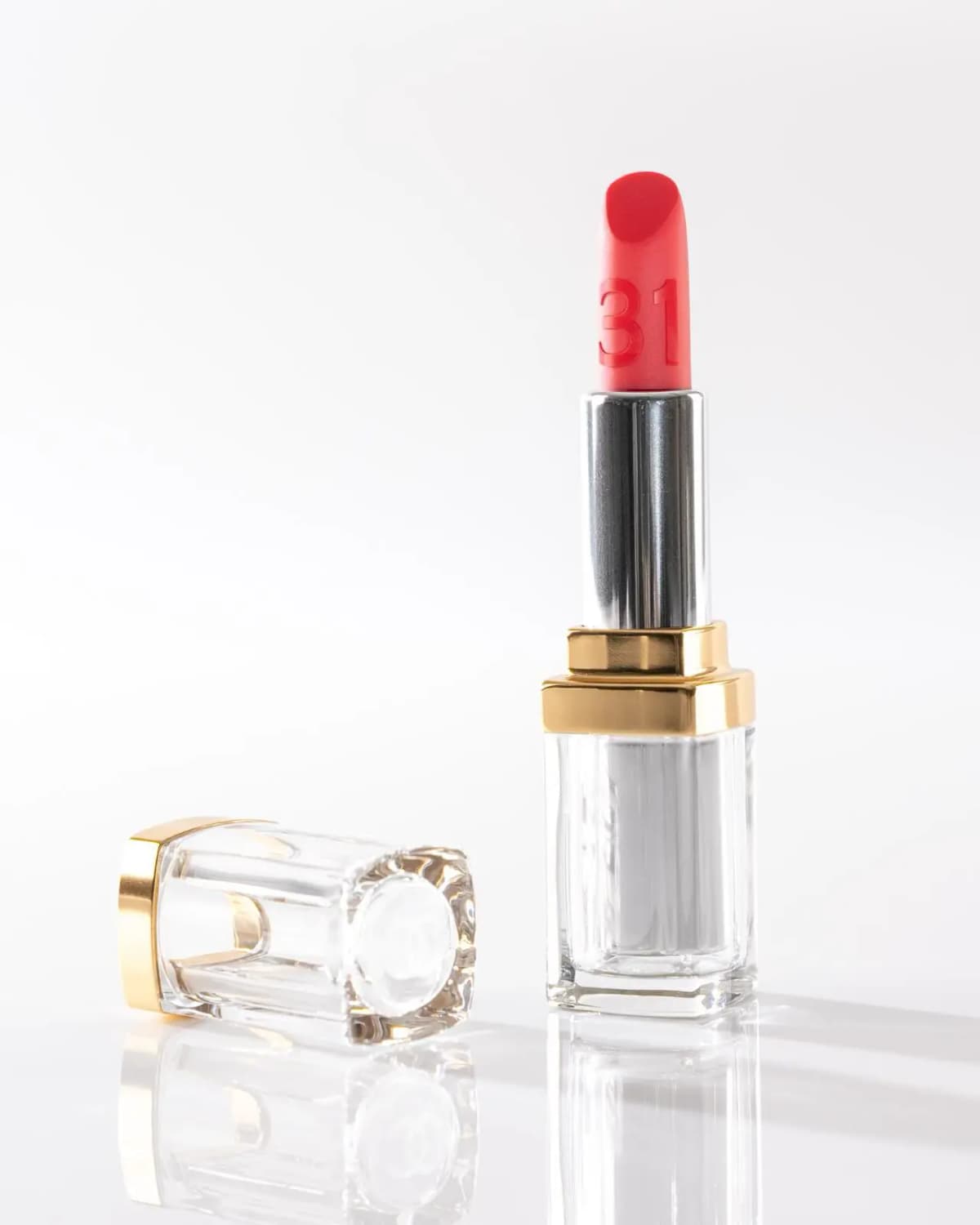 Chanel 31 Le Rouge Supreme Lip bright red shade No. 28 beside its clear gold-trimmed cap