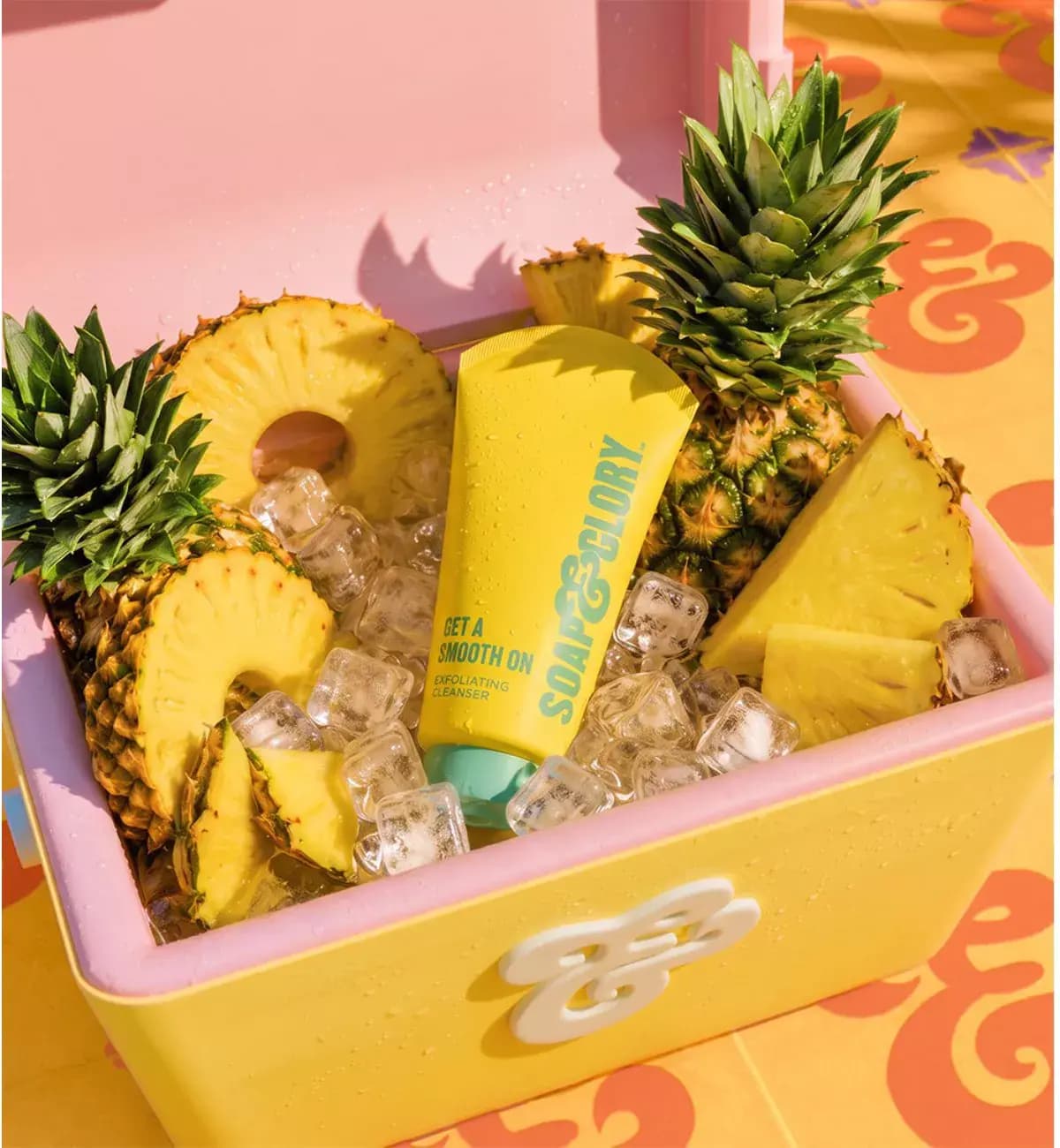 Yellow Get A Smooth On Exfoliating Cleanser tube on ice with pineapple slices in a pink and yellow cooler