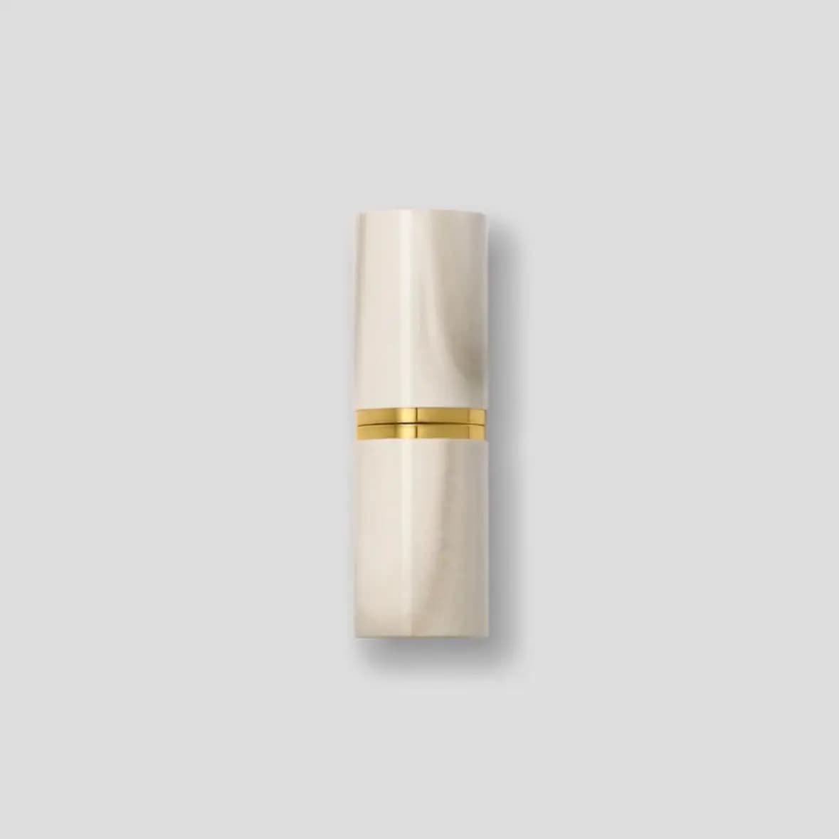 Closed lipstick case in white marbled finish with a polished gold band on a grey background