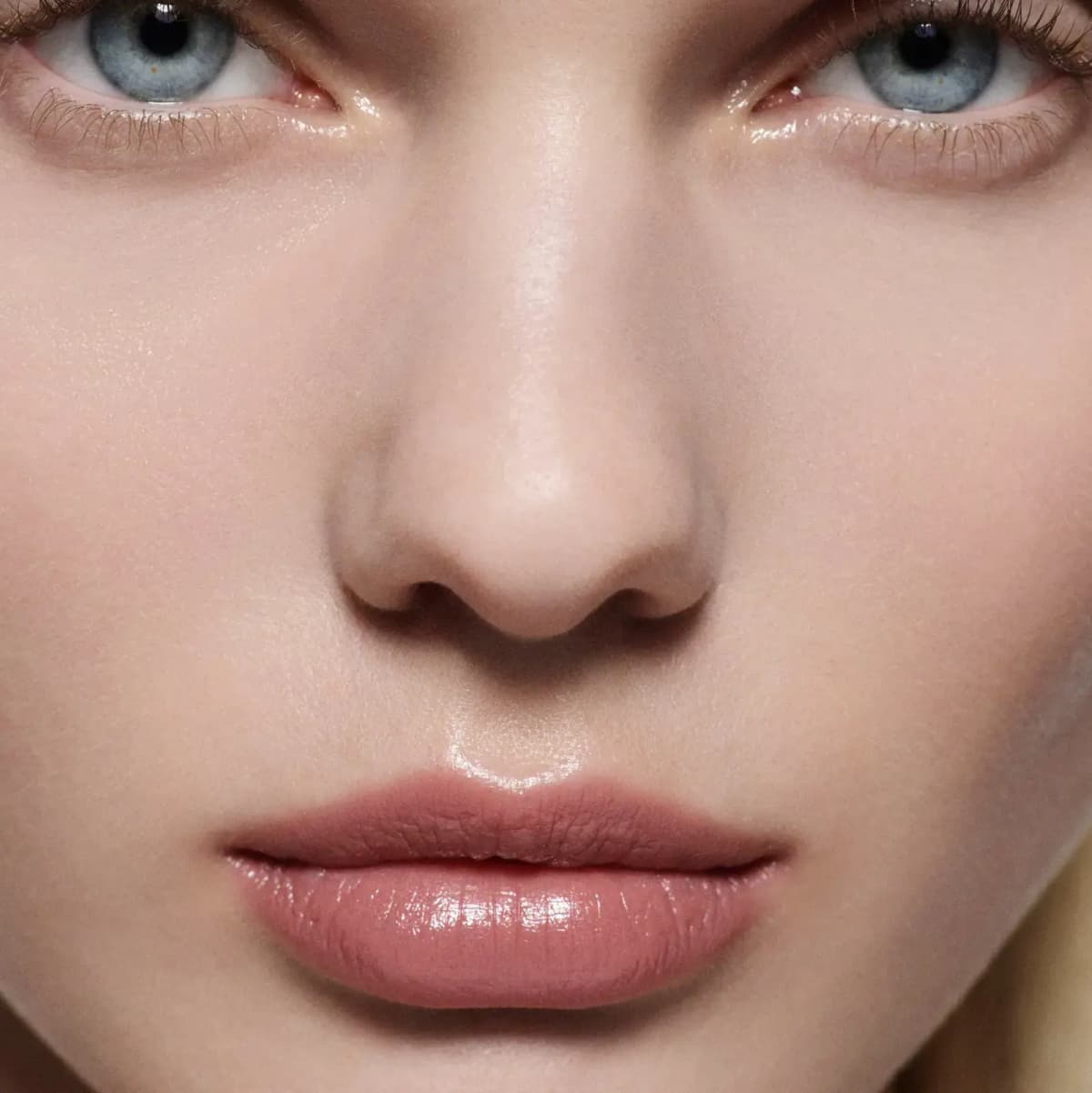 Close-up of glossy pink-nude lips on fair skin with pale blue eyes and dewy under-eye glow