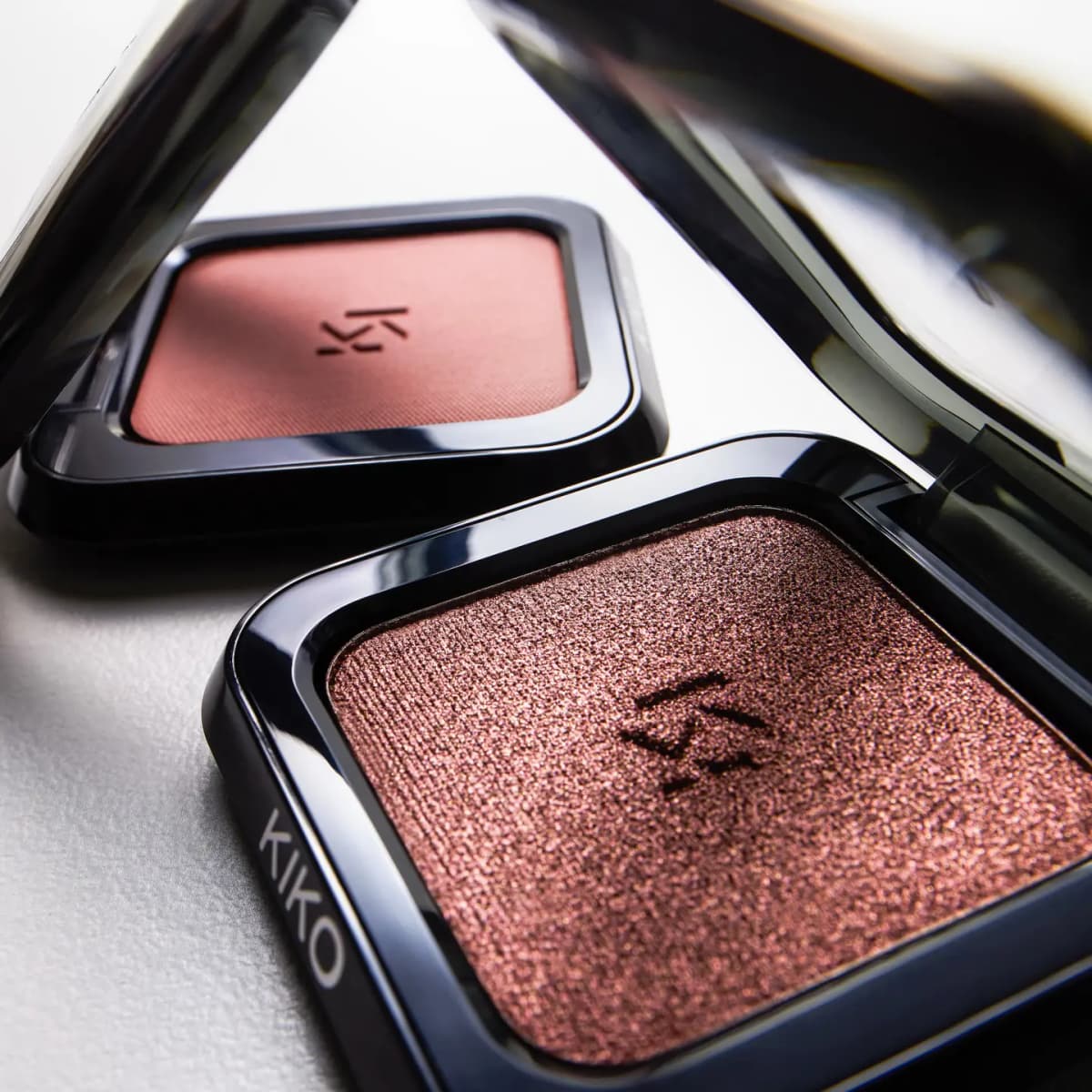 Close-up of two open KIKO eyeshadow compacts: a matte dusty rose shade and a shimmering metallic rosewood shade.