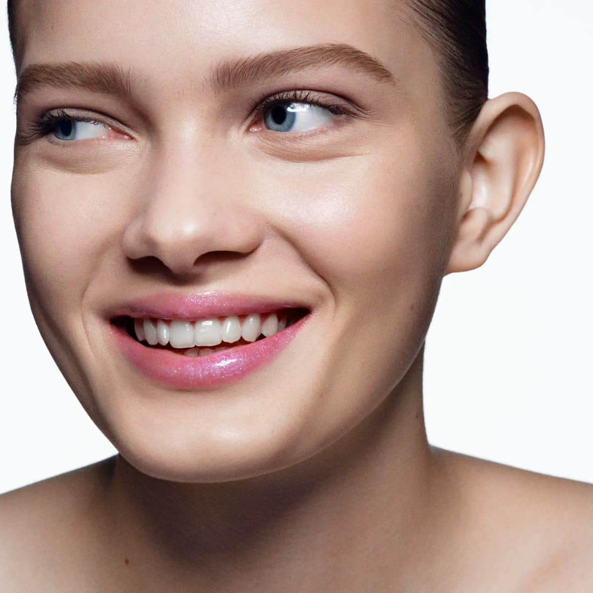 Smiling model wearing sheer pink gloss with iridescent blue sparkle on the lips