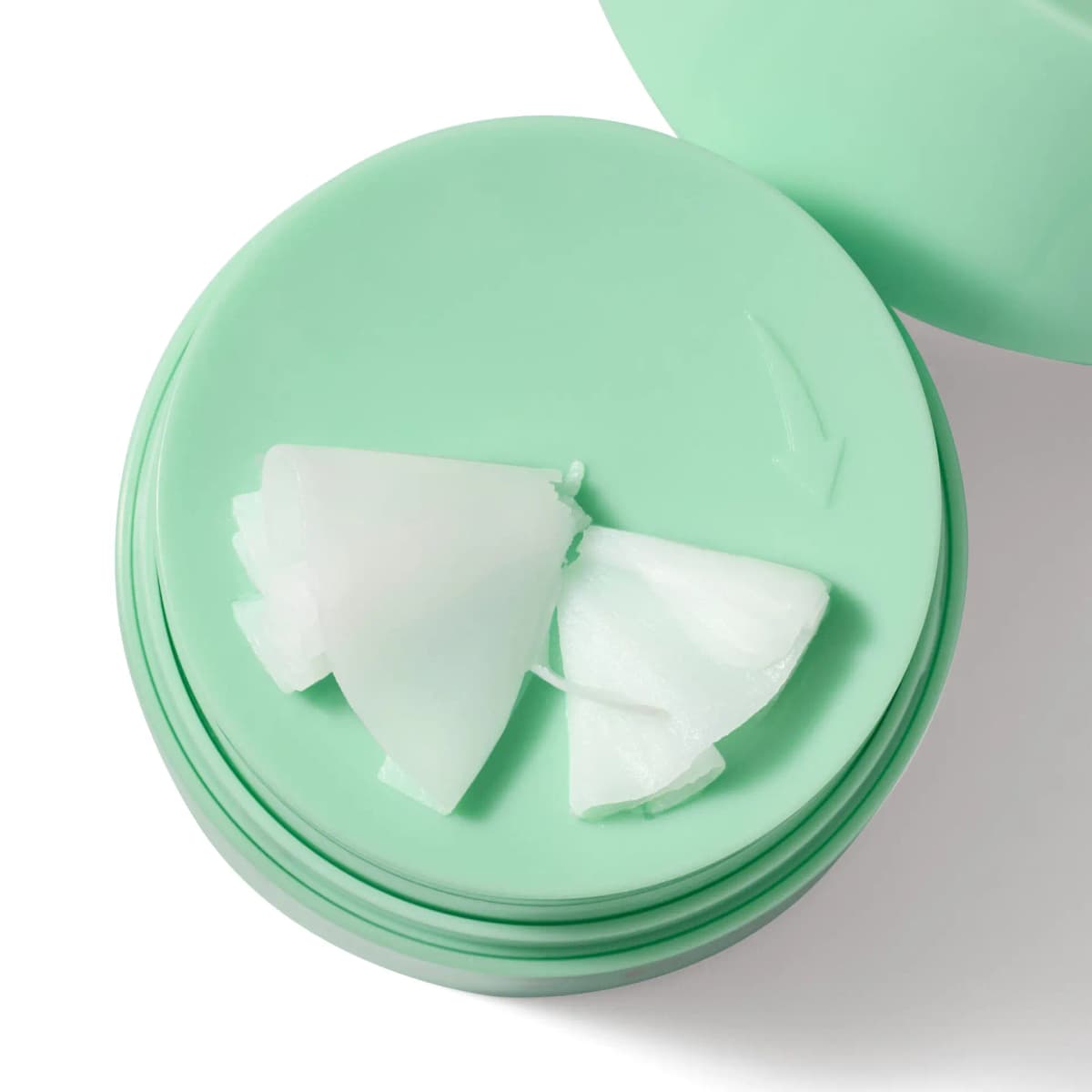 Open mint green jar with white cleansing balm curls on a twist-to-dispense top marked with an arrow