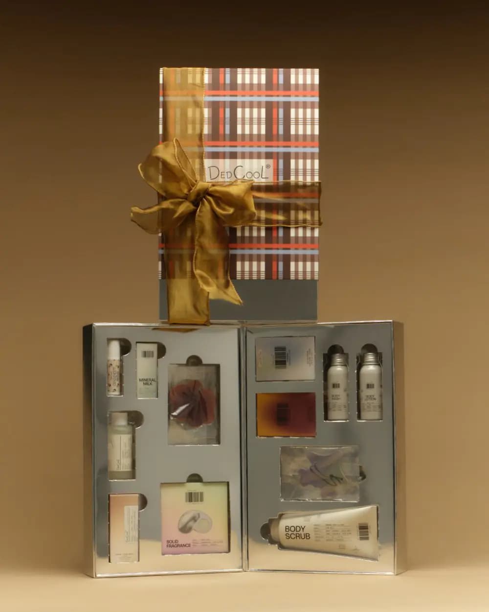 Plaid gift box tied with gold ribbon atop the open silver tray showing body scrub, solid fragrance and minis